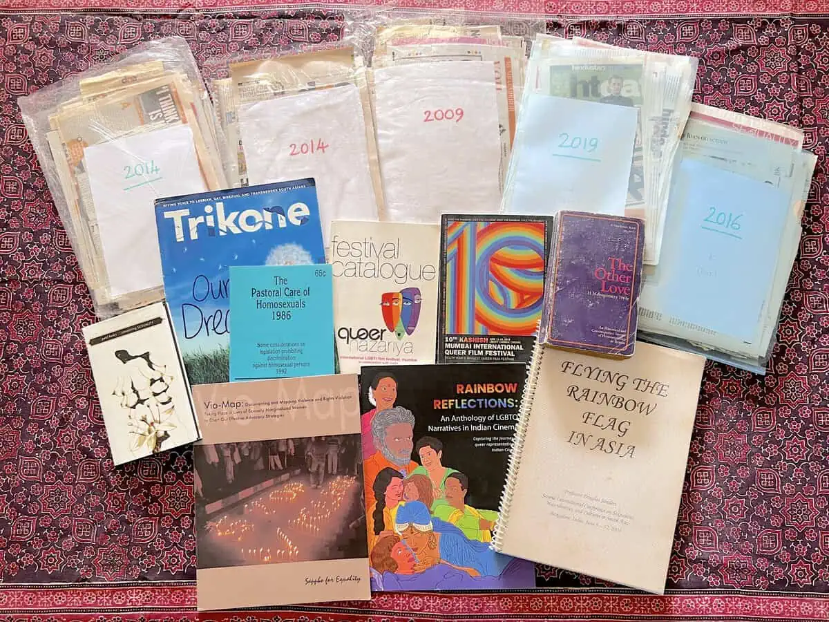 Archived queer publications and dated bundles of press clippings laid out on a printed cloth.