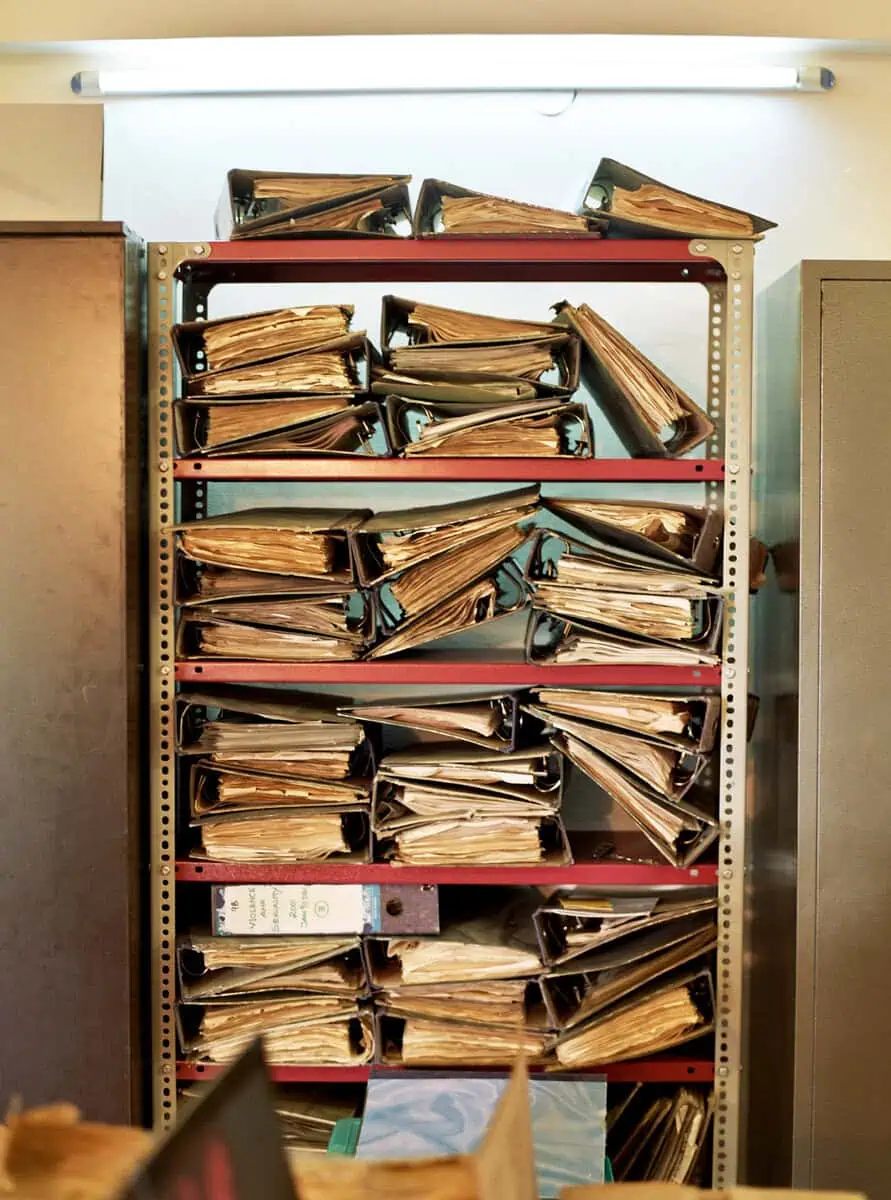 A metal shelf packed with overflowing ring binders of archived documents.