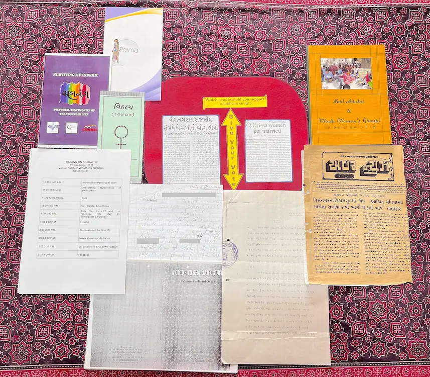 Pamphlets, workshop schedules and Gujarati-language clippings on sexuality and gender laid out on a printed cloth.