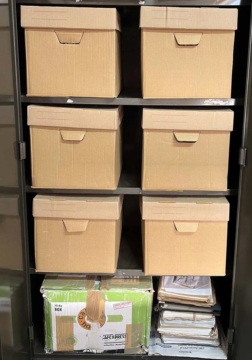 Archival storage boxes stacked on the shelves of a metal cabinet.